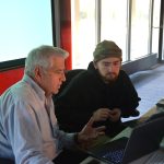 Professor George Giokas works with a student at a computer in the SoCJ's professional newsroom class