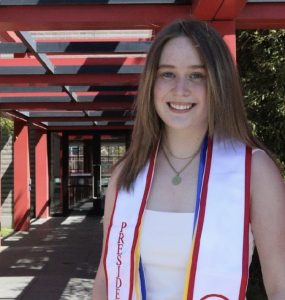 Lily McInerney wears her graduation stoles. The Stony Brook Wang Center is behind her.