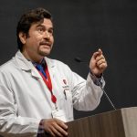 Male doctor in a white coat giving a lecture at a podium with a microphone